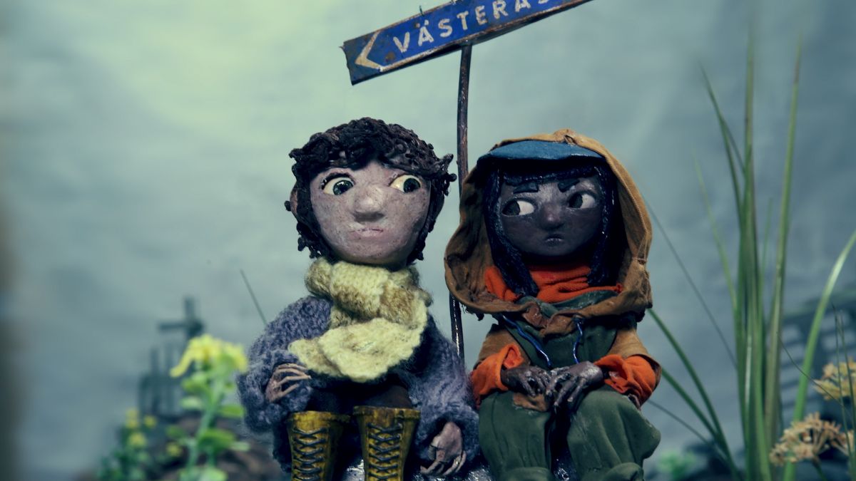 Tv&aring; lerfigurer sitter bredvid varandra framf&ouml;r en v&auml;gskylt med orten V&auml;ster&aring;s.