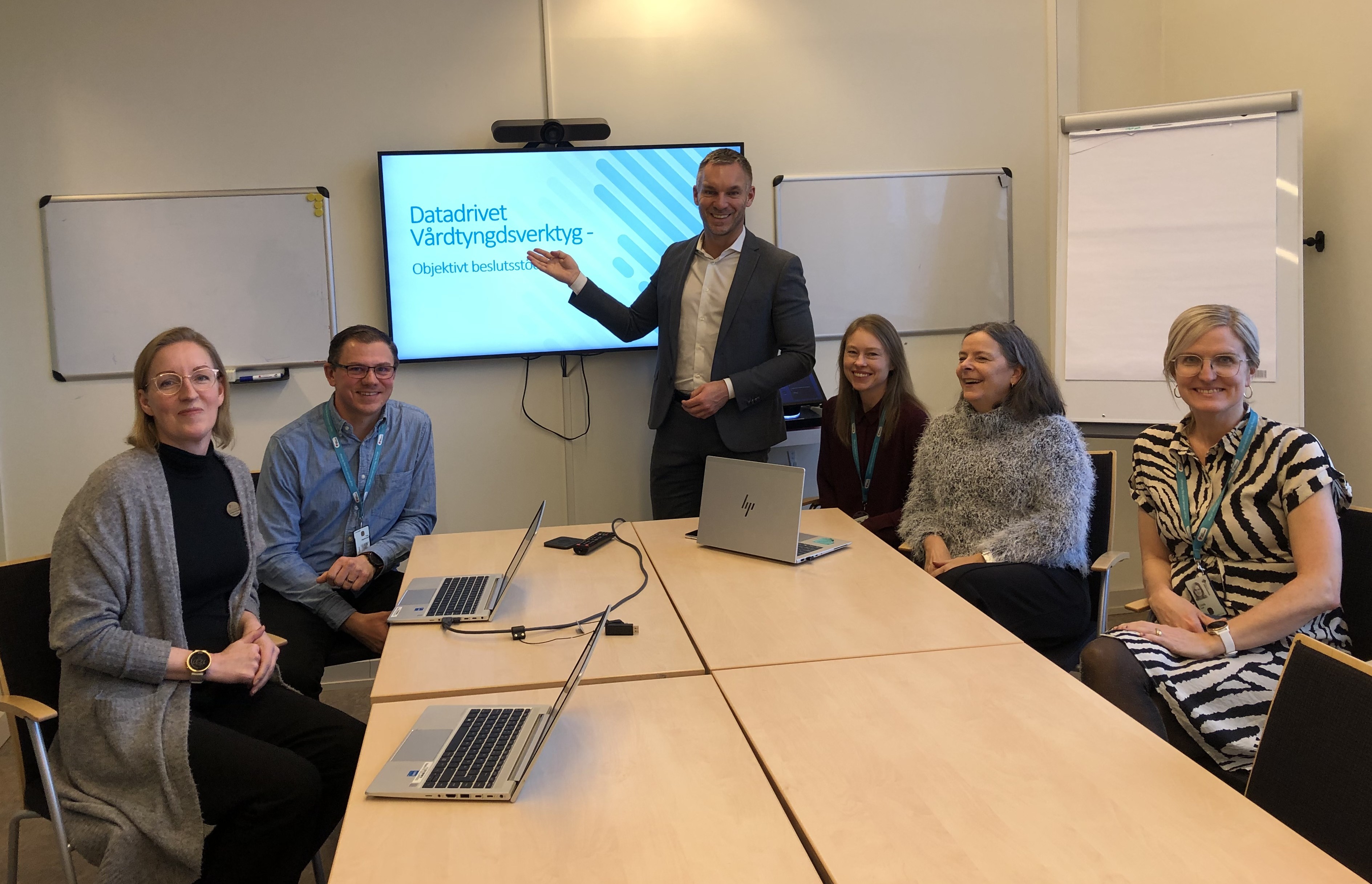 Ses personer i ett sammanträdesrum framför en presentation.