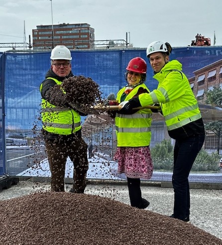 Tre personer gräver med en gemensam spade i en grushög.