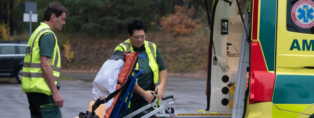 Två ambulanssjuksköterskor lyfter in en bår i en ambulans.