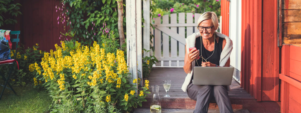 En kvinna sitter på en veranda och använder en bärbar dator