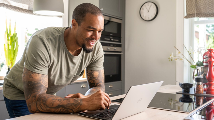 En man står med sin laptop vid en köksö