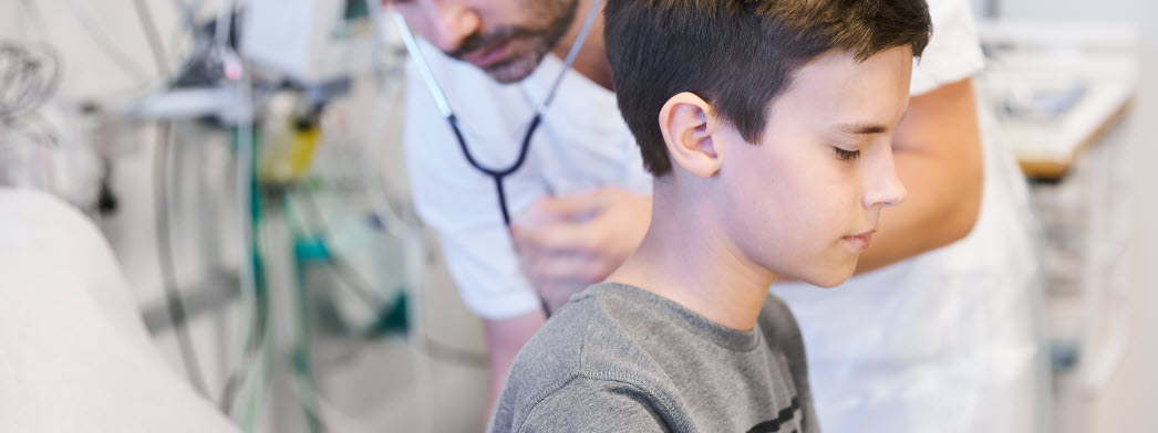 Ett barn sitter i bild och en läkare med stetoskop står i bakgrunden.