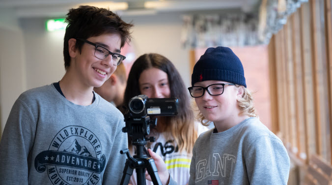 Tre ungdomar står bakom en filmkamera i skolmiljö