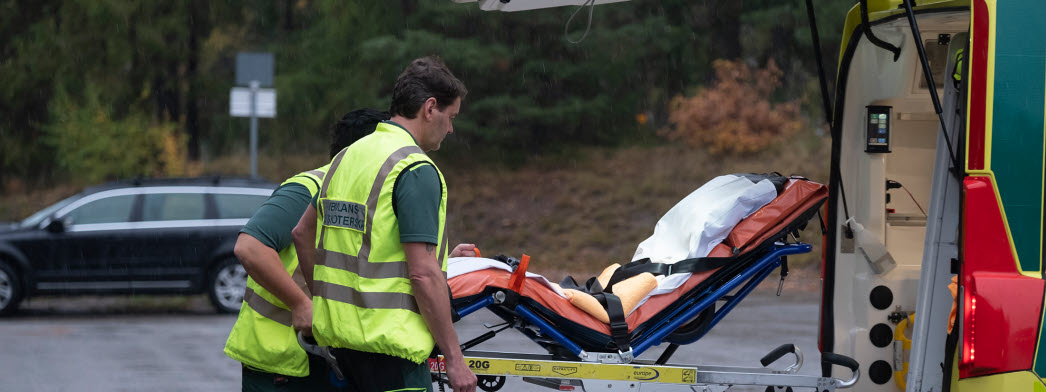Två ambulanssjuksköterskor lyfter in en bår i en ambulans.