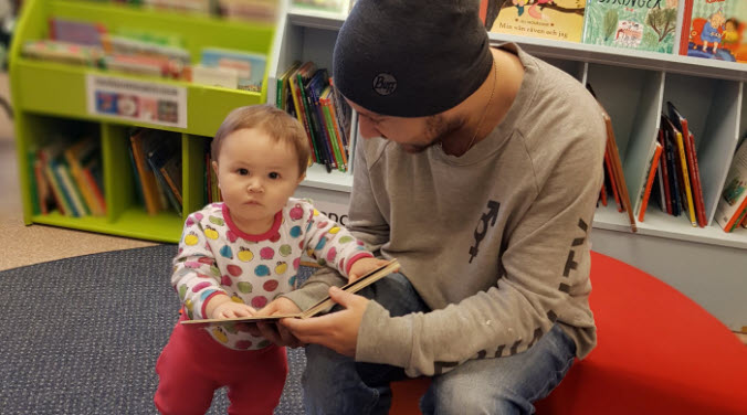 Pappa med barn läser bok på bibliotek