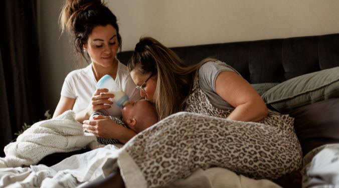 Två mammor matar sin bebis i sängen